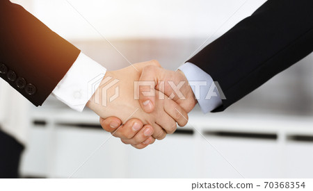 Businessman and woman shaking hands with colleagues at the background. Handshake at meeting in sunny office 70368354