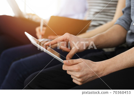 Group of casual dressed business people working at meeting or conference in sunny office, close-up of hands. Businessman using tablet computer Group of casual dressed business people working at meeting or conference in sunny office, close-up of hands. Businessman using tablet computer 70368453