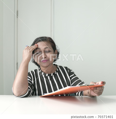 Businesswoman holding a file and a hand on her head Businesswoman holding a file and a hand on her head 70371401