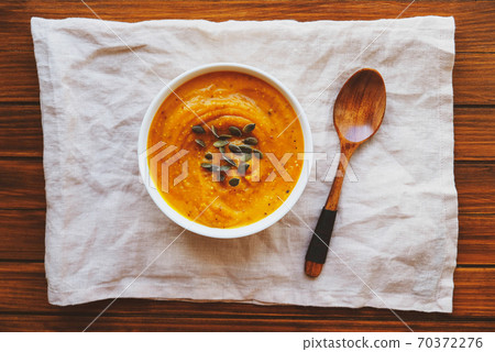 Hot pumpkin soup served with squash seeds in a bowl on wooden background. 70372276