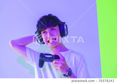 [Image of e-sports] A male gamer who is excited with a controller in one hand under purple and green lighting 70378241