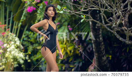 Beautiful young asian woman in black color bikini posing in tropical garden. Summer fashion and vacation 70379735