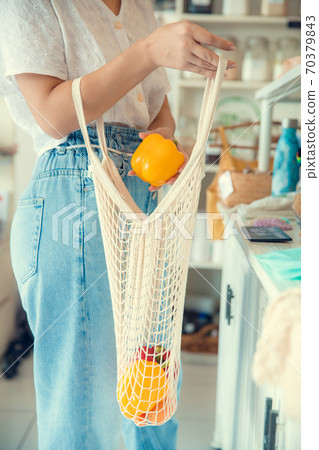 Woman hand holding string shopping bag with vegetables and fruits in eco shop. Vegetables in eco-friendly string reusable net mesh bag. Zero waste. New alternative buying Woman hand holding string shopping bag with vegetables and fruits in eco shop. Vegetables in eco-friendly string reusable net mesh bag. Zero waste. New alternative buying 70379843
