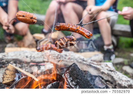 Friends roast sausages over an open fire outdoors 70382970