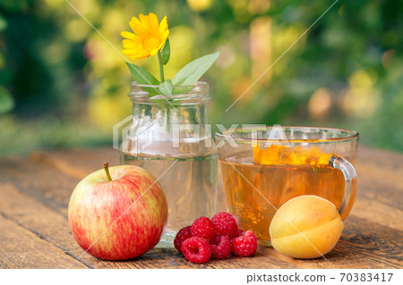 Ripe fruits, calendula flower with a stem in a glass jar and cup of greeen tea Ripe fruits, calendula flower with a stem in a glass jar and cup of greeen tea 70383417
