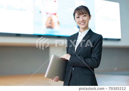 A young business woman standing with a PC in front of a large vision 70385212