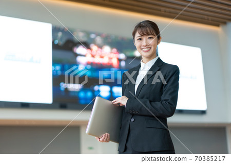 A young business woman standing with a PC in front of a large vision 70385217
