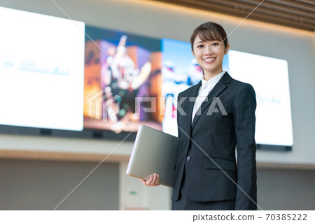 A young business woman standing with a PC in front of a large vision A young business woman standing with a PC in front of a large vision 70385222