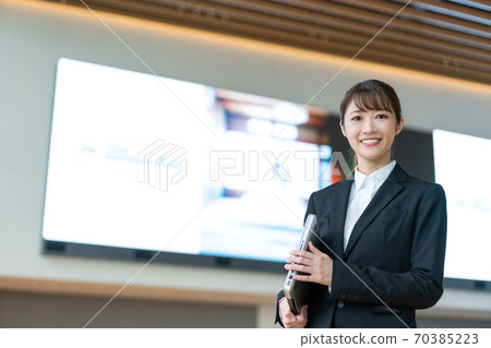 A young business woman standing with a PC in front of a large vision A young business woman standing with a PC in front of a large vision 70385223