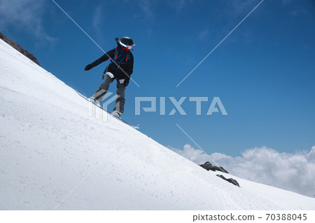 Girl snowboarder with a backpack on a snowy fresh slope against the backdrop of high mountains and blue sky. Winter kinds of extreme sports. Snowboard 70388045