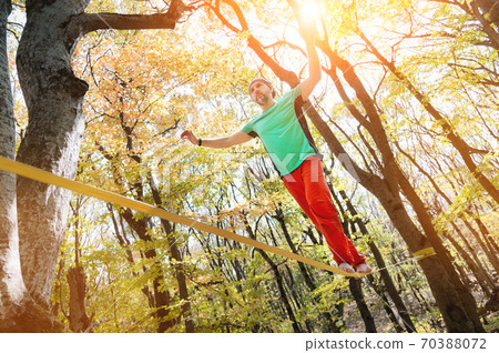 A bearded man in age walks along a slackline stretched in an autumn forest. Active recreation for middle-aged people A bearded man in age walks along a slackline stretched in an autumn forest. Active recreation for middle-aged people 70388072