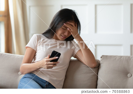 Upset young Asian woman crying, holding phone, received bad message 70388863