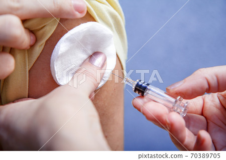 Hand of doctor holding syringe for vaccination to upper arm of patient Hand of doctor holding syringe for vaccination to upper arm of patient 70389705
