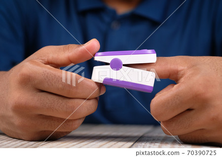 Close up of young man's hand using pulse oximeter 70390725