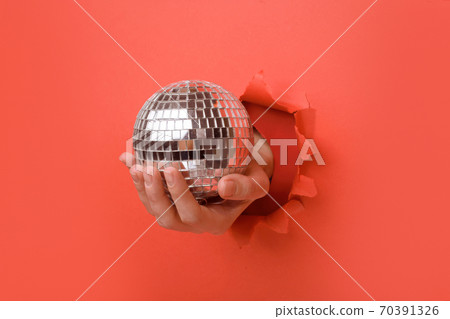 Hand holding Silver disco mirror ball on torn red paper wall. Copy space aside for your advertising and offer or sale content. 70391326