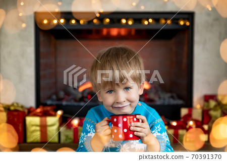 Happy child with cup of milk against fireplace Happy child with cup of milk against fireplace 70391370