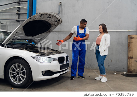 A repairer shows the client the engine of a car A repairer shows the client the engine of a car 70393789