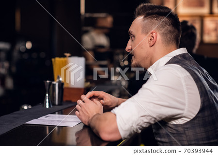a young man in a shirt and vest makes an order from the menu at the bar 70393944