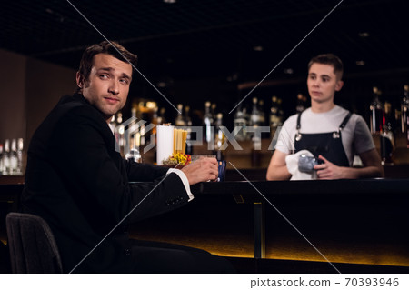 a young man drinks a cocktail at the bar, communicates with the bartender a young man drinks a cocktail at the bar, communicates with the bartender 70393946