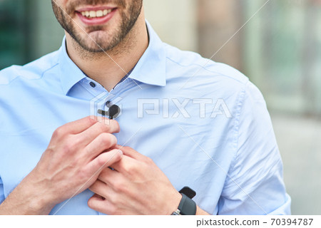 Young handsome man, male blogger adjusting small lavalier microphone on his shirt and smiling while standing outdoors Young handsome man, male blogger adjusting small lavalier microphone on his shirt and smiling while standing outdoors 70394787