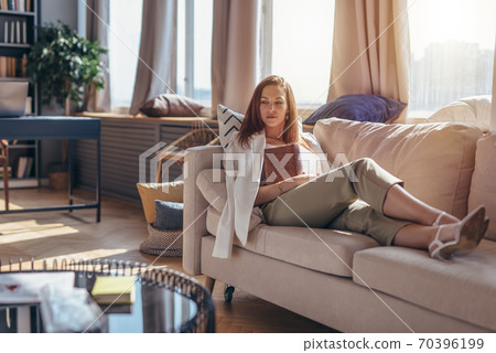 Young woman at home lying on sofa with a book. 70396199