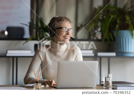 Smiling female employee in headphones laugh talking on video call 70396352
