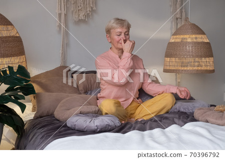 Senior woman practicing yoga at home, making Alternate Nostril Breathing exercise, nadi shodhana pranayama Senior woman practicing yoga at home, making Alternate Nostril Breathing exercise, nadi shodhana pranayama 70396792