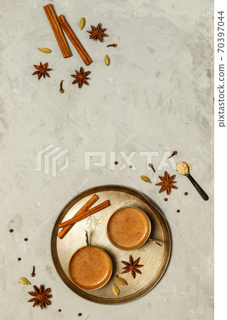 Hot fragrant masala tea in small copper cups on a round tray.On a grey stone background with spices, top view with space 70397044