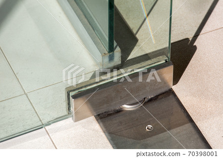 Glass door fittings, swivel mechanism holding the door metal loop on the tile floor close up. Glass door fittings, swivel mechanism holding the door metal loop on the tile floor close up. 70398001