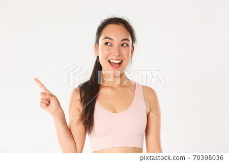 Sport, wellbeing and active lifestyle concept. Cheerful smiling asian sportswoman in sportsbra, looking amazed and happy, making her choice, pointing and looking upper left corner Sport, wellbeing and active lifestyle concept. Cheerful smiling asian sportswoman in sportsbra, looking amazed and happy, making her choice, pointing and looking upper left corner 70398036