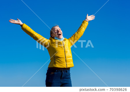 a joyful girl hands up, took off the mask from his smiling face and enjoys the fresh air in freedom against a blue sky with copy space. 70398626