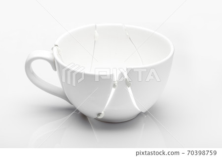 white ceramic cup broken into fragments as a result of the fall and glued chewing gum in the hope of salvation, a concept of a kitchen object on the theme of crisis on a white background. white ceramic cup broken into fragments as a result of the fall and glued chewing gum in the hope of salvation, a concept of a kitchen object on the theme of crisis on a white background. 70398759
