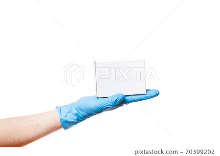 Delivery man's hand in a blue sterile latex glove holds a white unlabel cardboard box on palm, safe delivery during quarantine stay home, isolated on a white background with copy space. Delivery man's hand in a blue sterile latex glove holds a white unlabel cardboard box on palm, safe delivery during quarantine stay home, isolated on a white background with copy space. 70399202