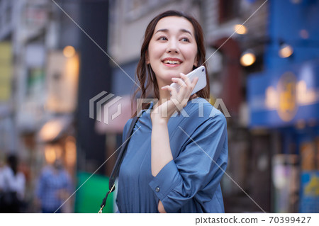A woman holding a smartphone on the street corner at dusk 70399427