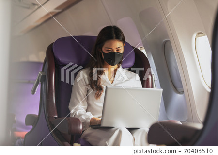 Asian young woman wearing protective mask using laptop sitting near windows at first class on airplane during flight,Traveling and Business during COVID-19 virus pandemic concept Asian young woman wearing protective mask using laptop sitting near windows at first class on airplane during flight,Traveling and Business during COVID-19 virus pandemic concept 70403510