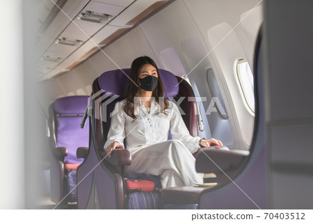 Asian young woman wearing protective mask sitting near windows at first class on airplane during flight,Traveling and Business during COVID-19 virus pandemic concept Asian young woman wearing protective mask sitting near windows at first class on airplane during flight,Traveling and Business during COVID-19 virus pandemic concept 70403512