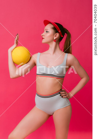 Portrait pretty flexible sport adult young girl flexible gymnast in retro swimsuit stand in attractive pose with ellow ball trapped in elbow isolated over pink vivid background looking aside Portrait pretty flexible sport adult young girl flexible gymnast in retro swimsuit stand in attractive pose with ellow ball trapped in elbow isolated over pink vivid background looking aside 70404039
