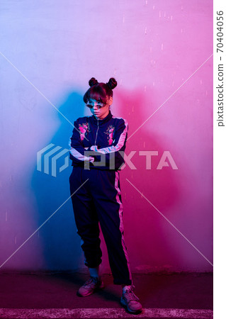 Woman in tracksuit with flower standing in neon light Woman in tracksuit with flower standing in neon light 70404056