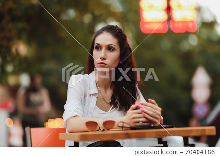 Woman sitting at a table on the street. Evening warm city. Woman sitting at a table on the street. Evening warm city. 70404186