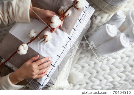 Woman hand holding a cotton branch with stack of folded linens near rolled up towels in mesh basket Woman hand holding a cotton branch with stack of folded linens near rolled up towels in mesh basket 70404510