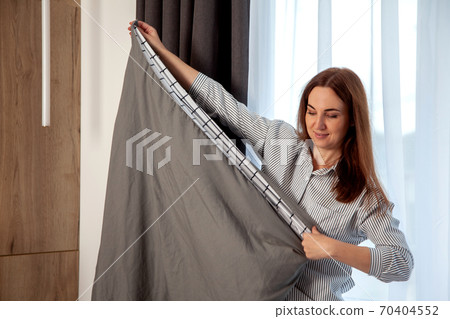Happy woman with long red hair is folding clean bedding set on the bed of room with copy space. 70404552