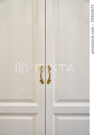 Classic white wardrobe with with ornamental golden handles close-up Classic white wardrobe with with ornamental golden handles close-up 70404875