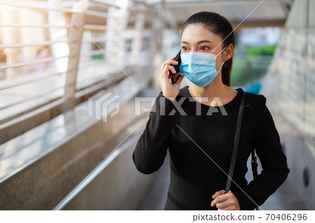 business woman talking with smartphone and wearing medical mask for protection from coronavirus (covid-19) pandemic in city 70406296