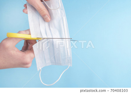 Man cuts a medical protective mask with yellow scissors on a blue background. Copyspace. The idea of conspiracy and disbelief in the danger of coronavirus Man cuts a medical protective mask with yellow scissors on a blue background. Copyspace. The idea of conspiracy and disbelief in the danger of coronavirus 70408103