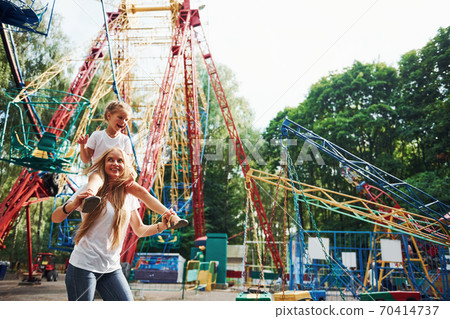Cheerful little girl her mother have a good time in the park together near attractions Cheerful little girl her mother have a good time in the park together near attractions 70414737