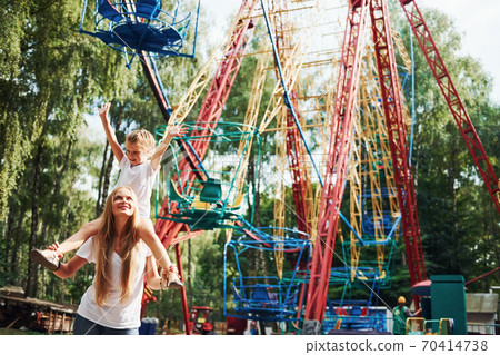 Cheerful little girl her mother have a good time in the park together near attractions Cheerful little girl her mother have a good time in the park together near attractions 70414738