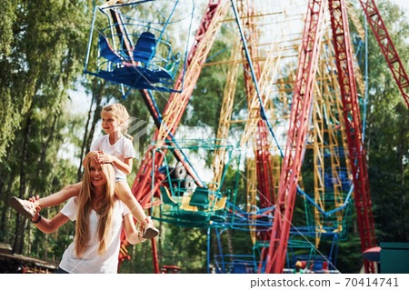 Cheerful little girl her mother have a good time in the park together near attractions 70414741