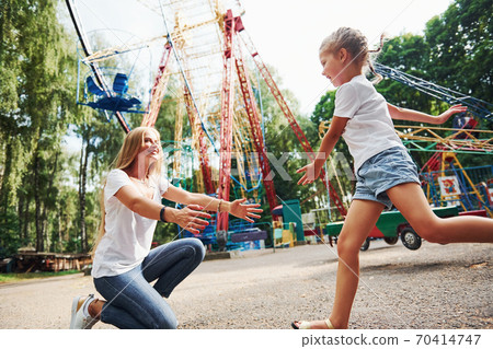 Running and playing. Cheerful little girl her mother have a good time in the park together near attractions 70414747