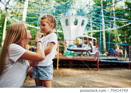 Loving each other. Cheerful little girl her mother have a good time in the park together near attractions Loving each other. Cheerful little girl her mother have a good time in the park together near attractions 70414749