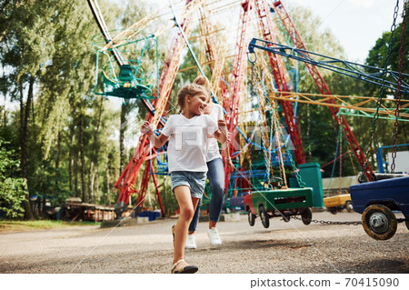 Running and playing. Cheerful little girl her mother have a good time in the park together near attractions 70415090